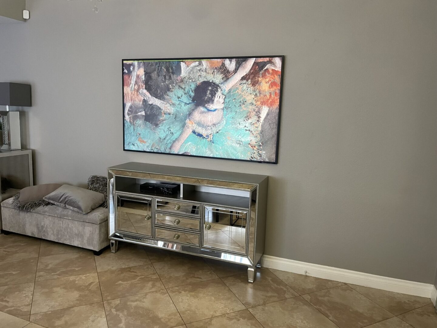 A television mounted on the wall above a mirrored dresser.