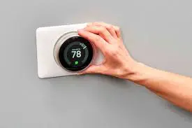 A hand adjusts a modern circular thermostat set to 78 degrees on a gray wall, showcasing the convenience of Smart Home Solutions.